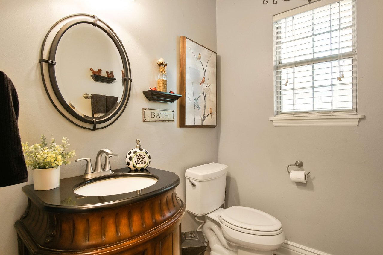 A bathroom with a unique, round vanity and sink. The room has a window, toilet, and is decorated with modern fixtures and artwork.