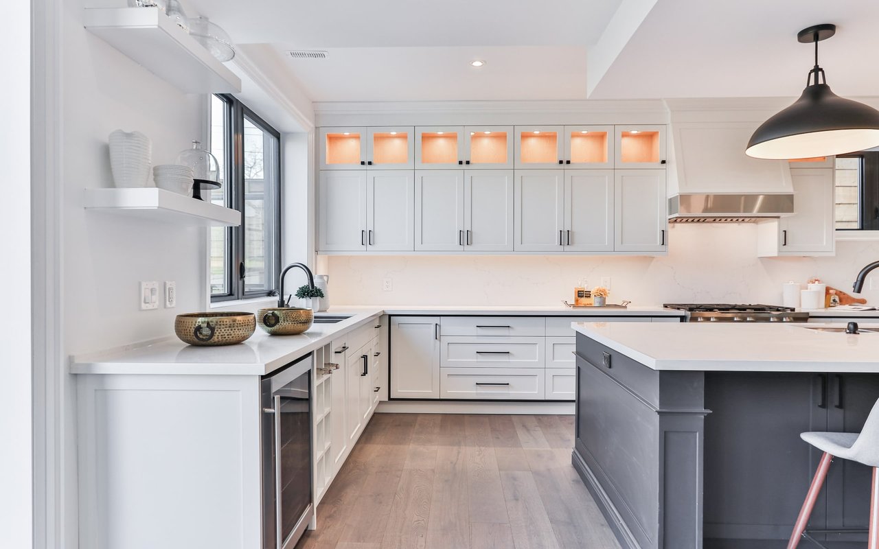 A modern kitchen with white cabinets, gray island, stainless steel appliances, island sink, wall stove, oven, and garden view.