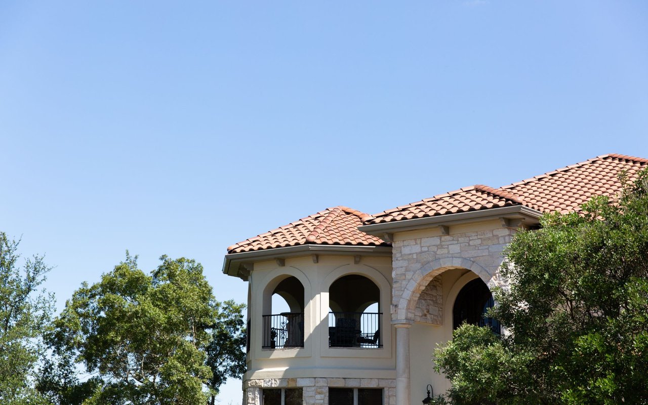 Home exterior with a terracotta tile roof, stone facade, and arched balcony openings.