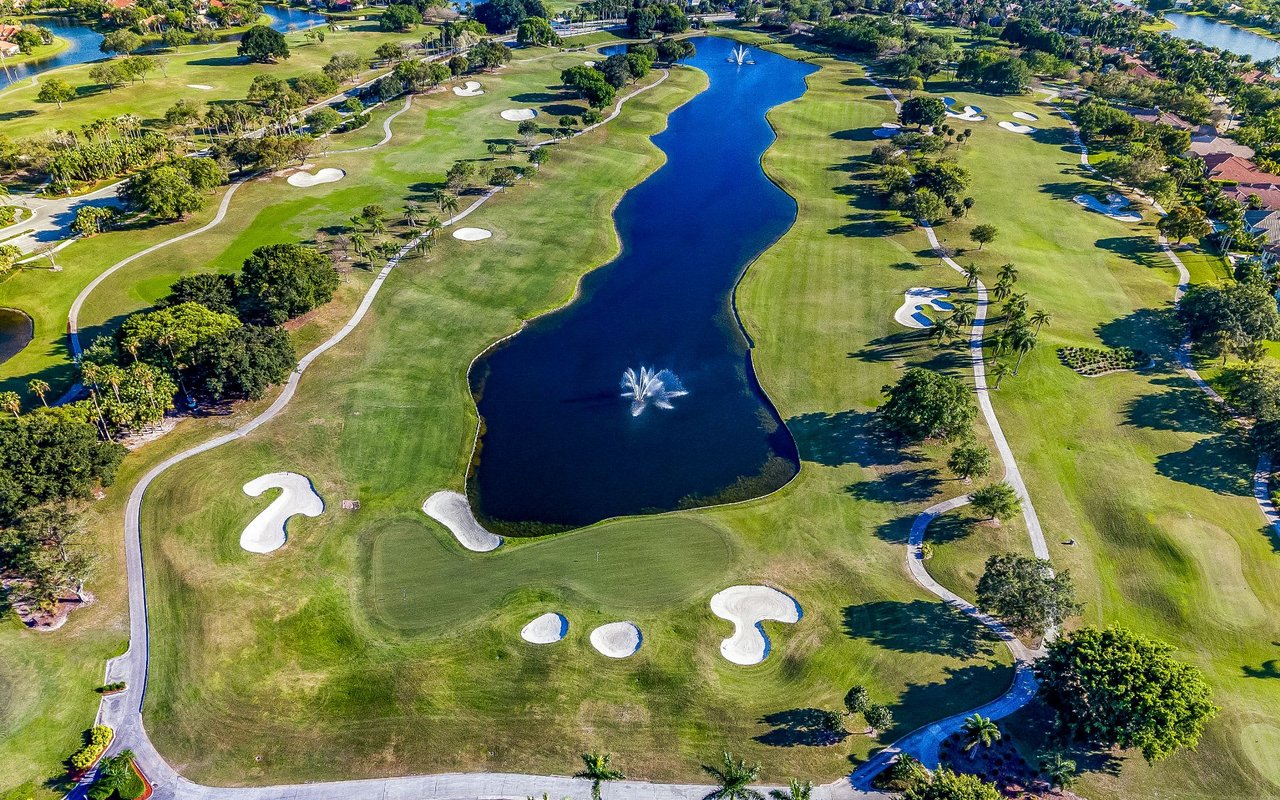 Weston homes for sale. Scenic aerial view capturing lush green fairways, sparkling blue lakes, and towering palm trees beneath the azure sky.