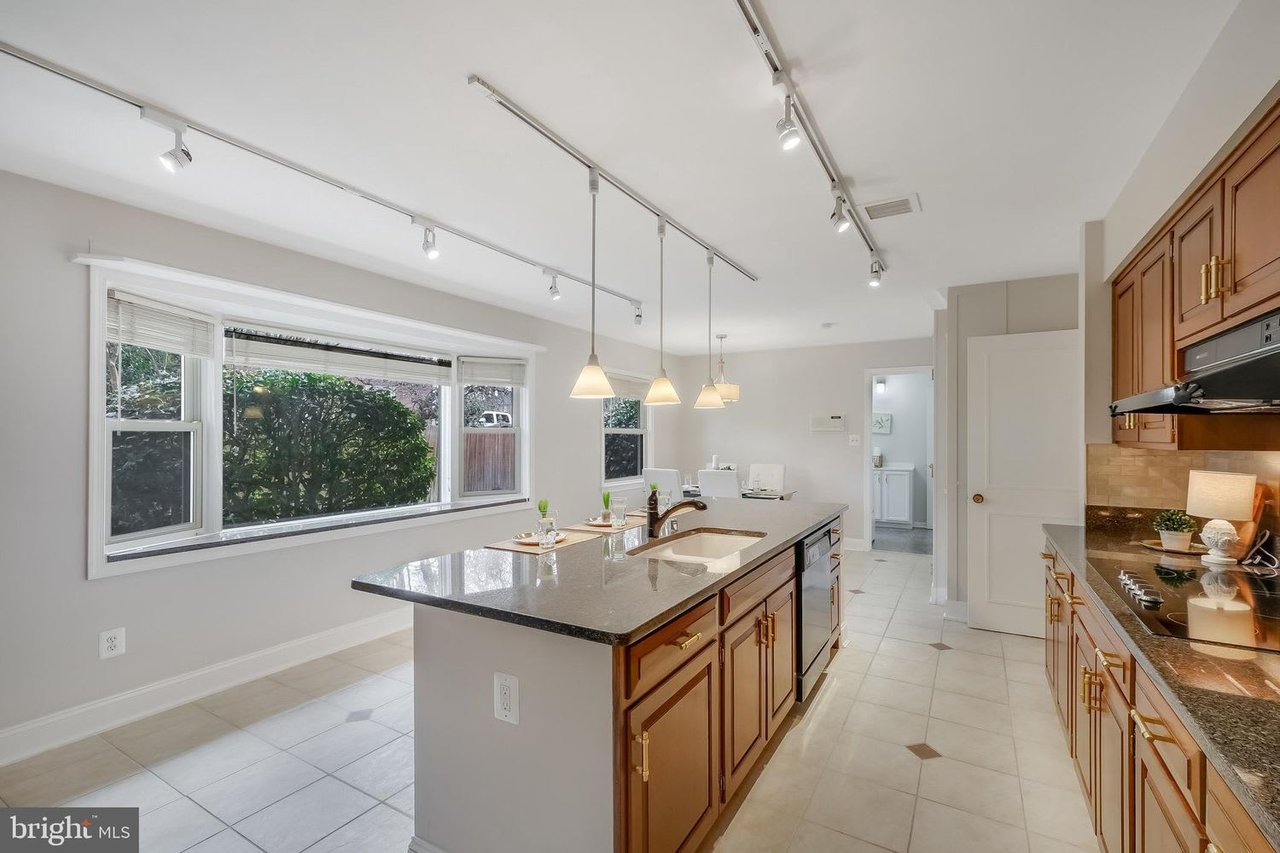 Kitchen with a long stone island, warm wood cabinets, pendant lights, and a wide window overlooking greenery.