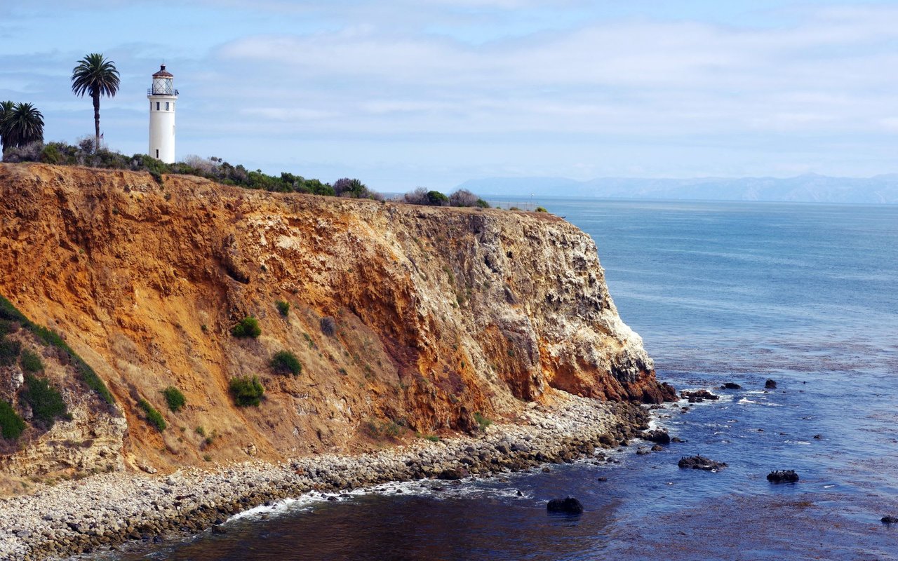 Sun-kissed cliffs and churning waves frame a solitary lighthouse, painting a picture of coastal serenity.