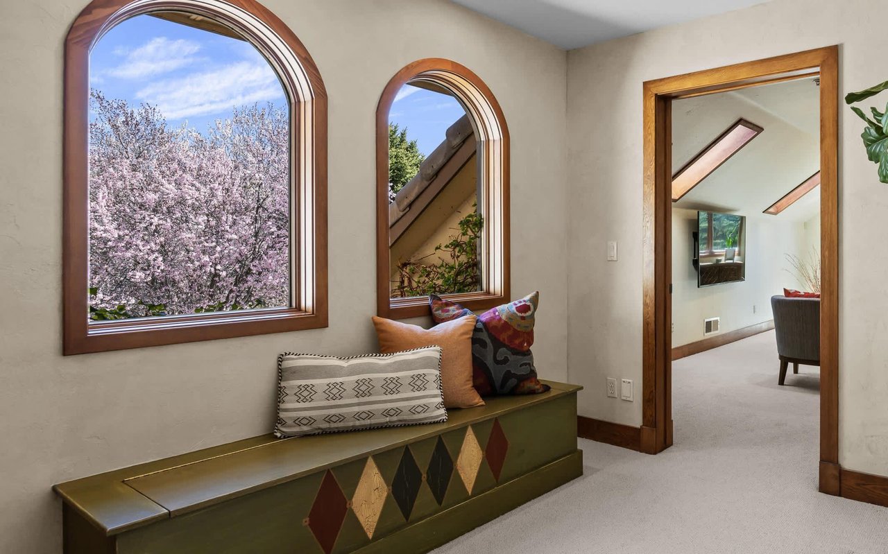 Reading nook below two large arched, wood-wrapped windows overlooking a cherry tree in full bloom.