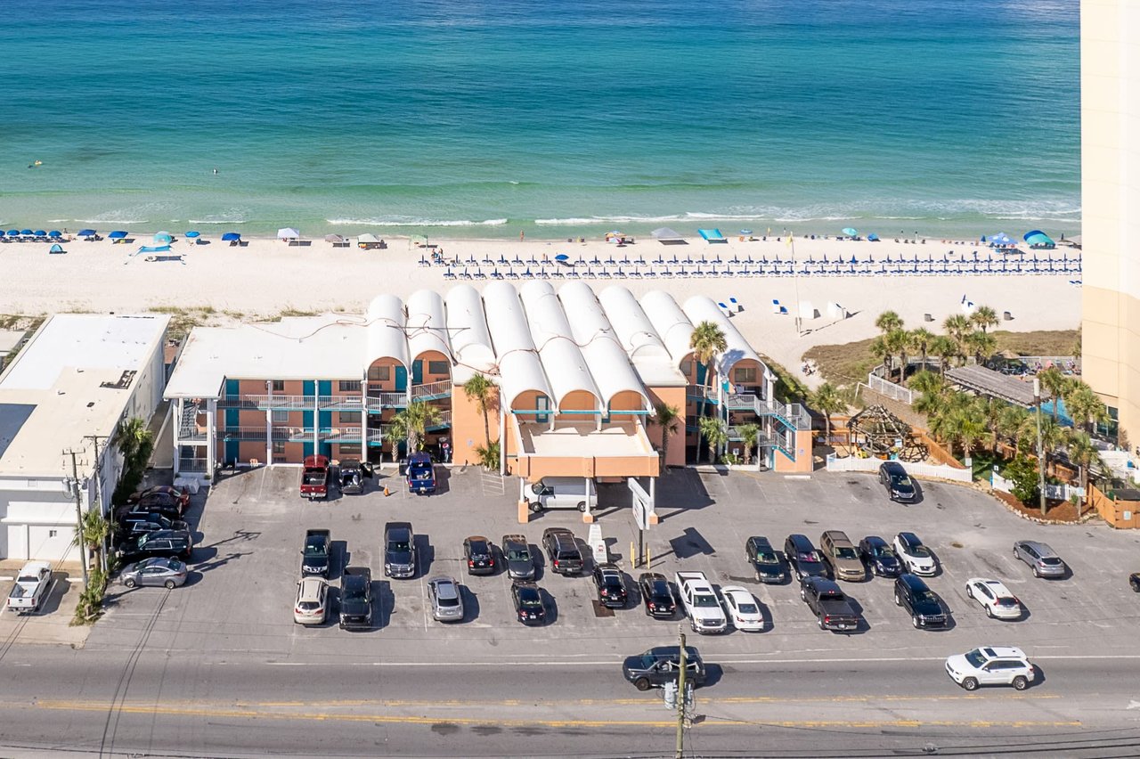 An aerial view of a beach resort with a parking lot beside the calm turquoise waters of the beach.