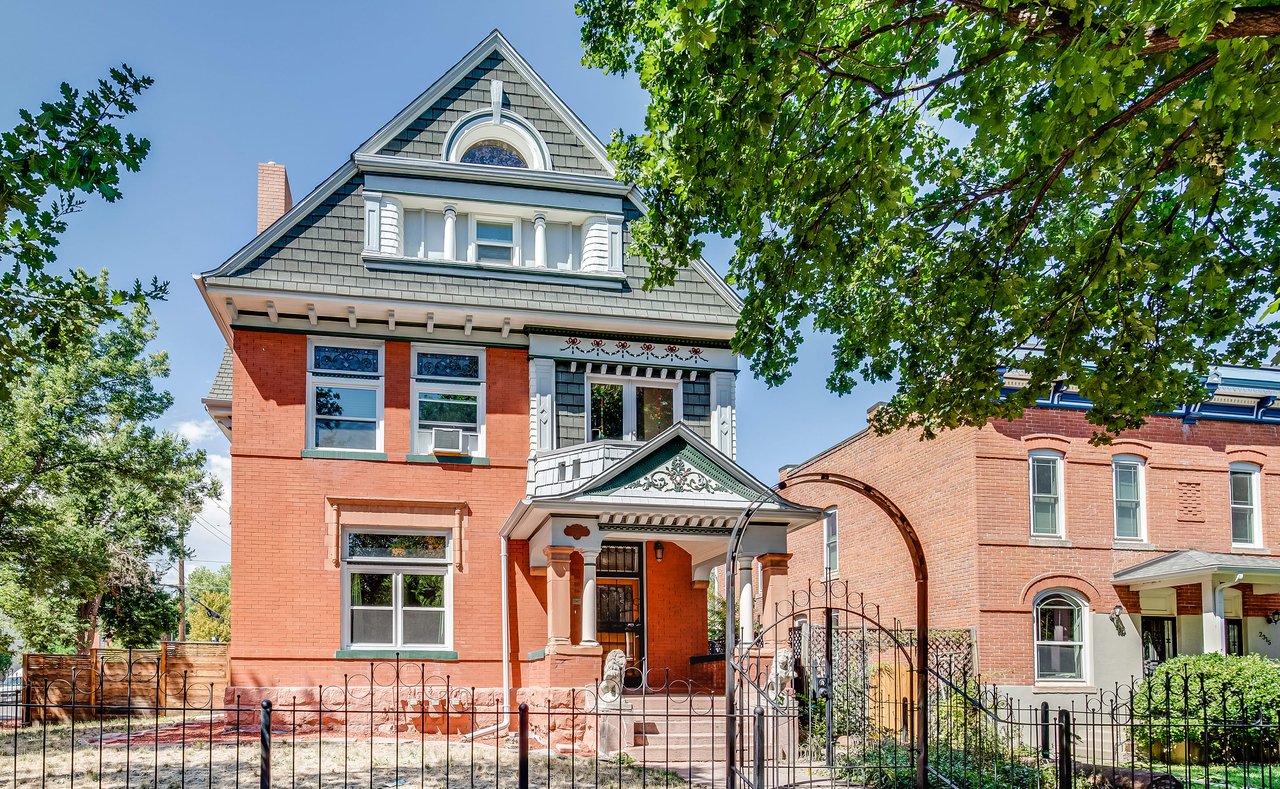 A charming red brick house with a green roof sits behind a wrought iron fence