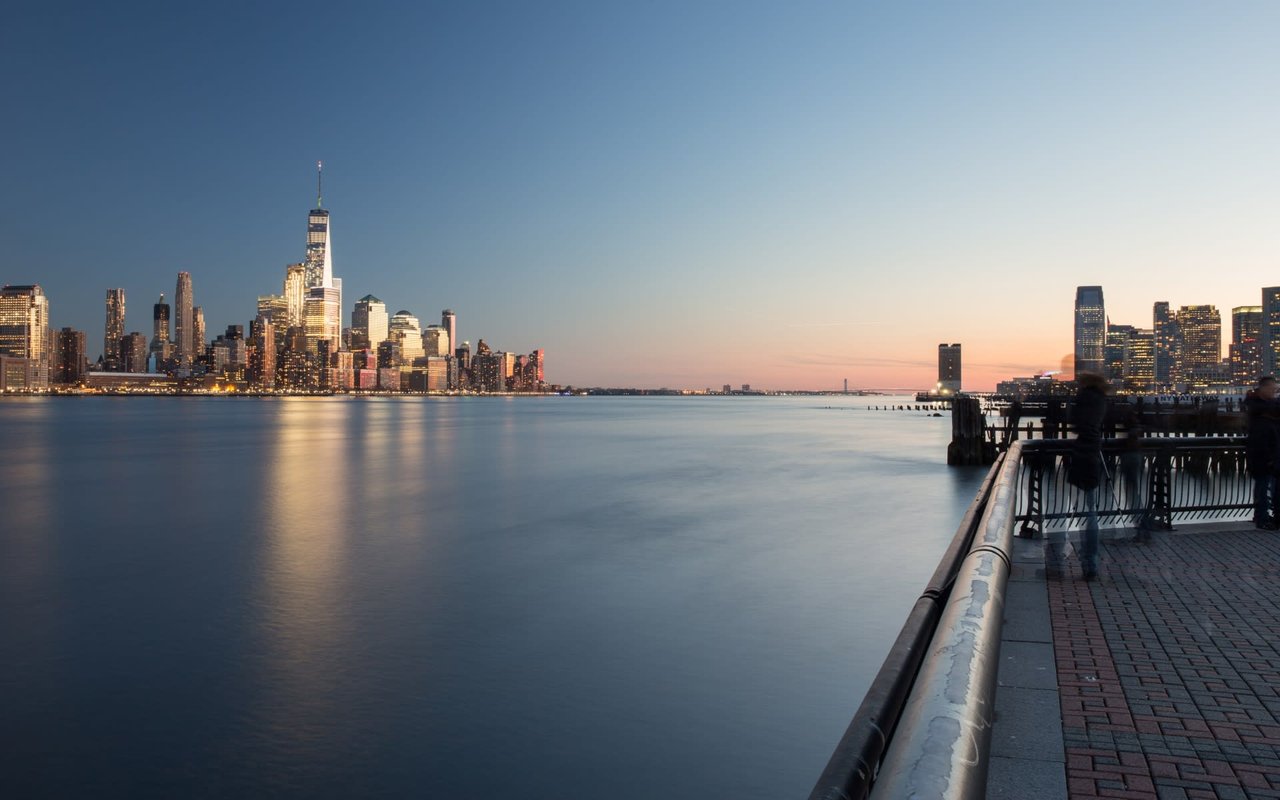 A skyline of high-rise and small buildings clustered together across the water at sunset.