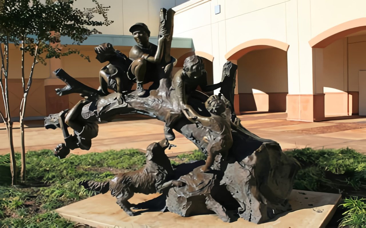 The sculpture is placed on a light-colored rectangular base surrounded by green groundcover.