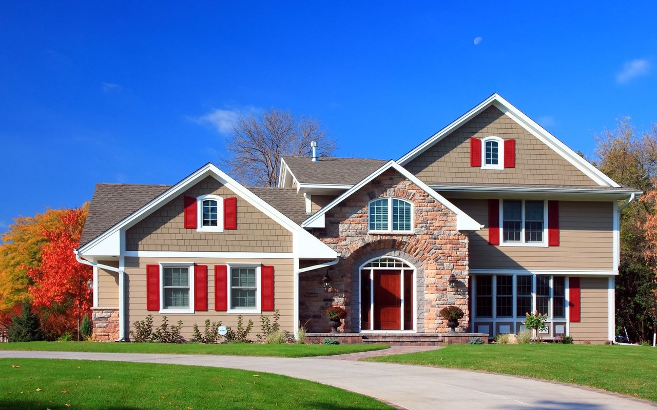 A two-story house with a beige exterior and red shutters.