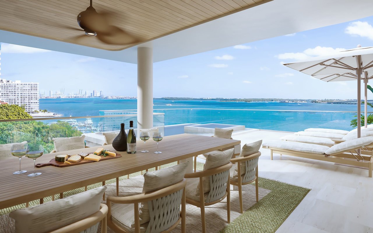 Furnished terrace overlooking Biscayne Bay, with a long dining table and white lounge chairs.