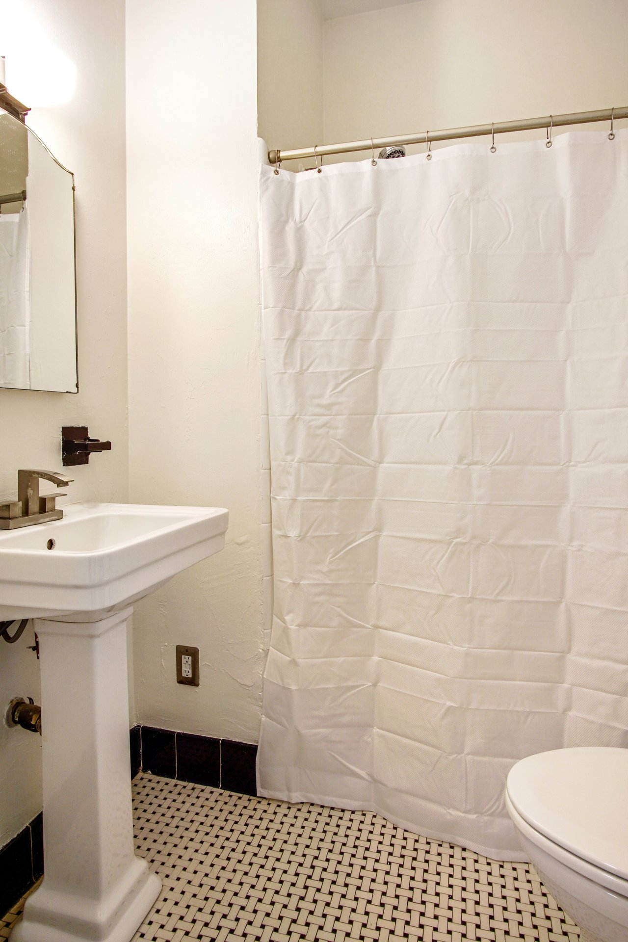 A bathroom with a sink, mirror, and shower/tub combo. The fixtures are modern, and the room has a clean, minimalist look.