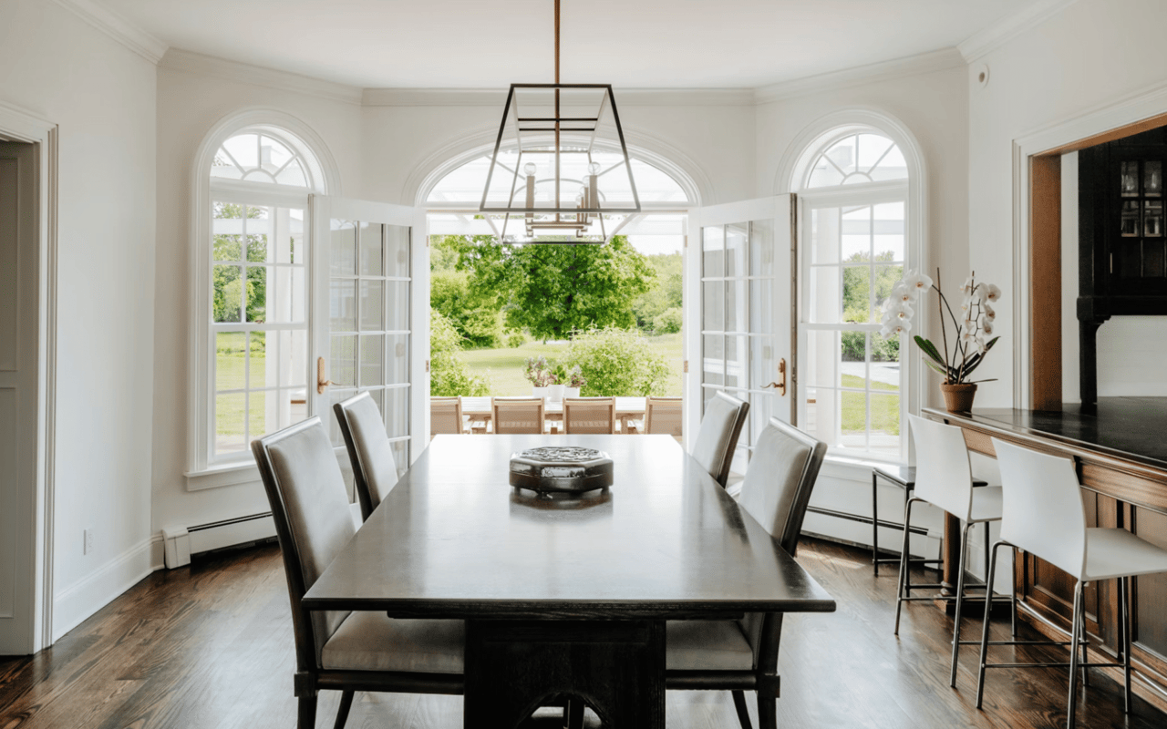  A luxurious dining room with dark wooden floors and white walls, bathed in natural light from multiple large arched windows.