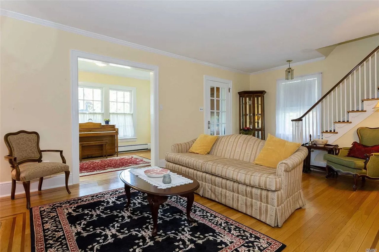 Furnished living room with a striped sofa, layered rugs, hardwood floors, and a staircase.