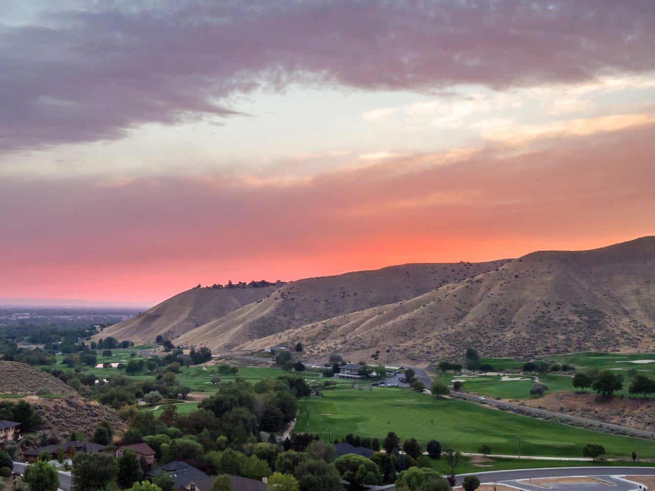 A lush green golf course winds through a valley, interspersed with residential areas and scattered trees.