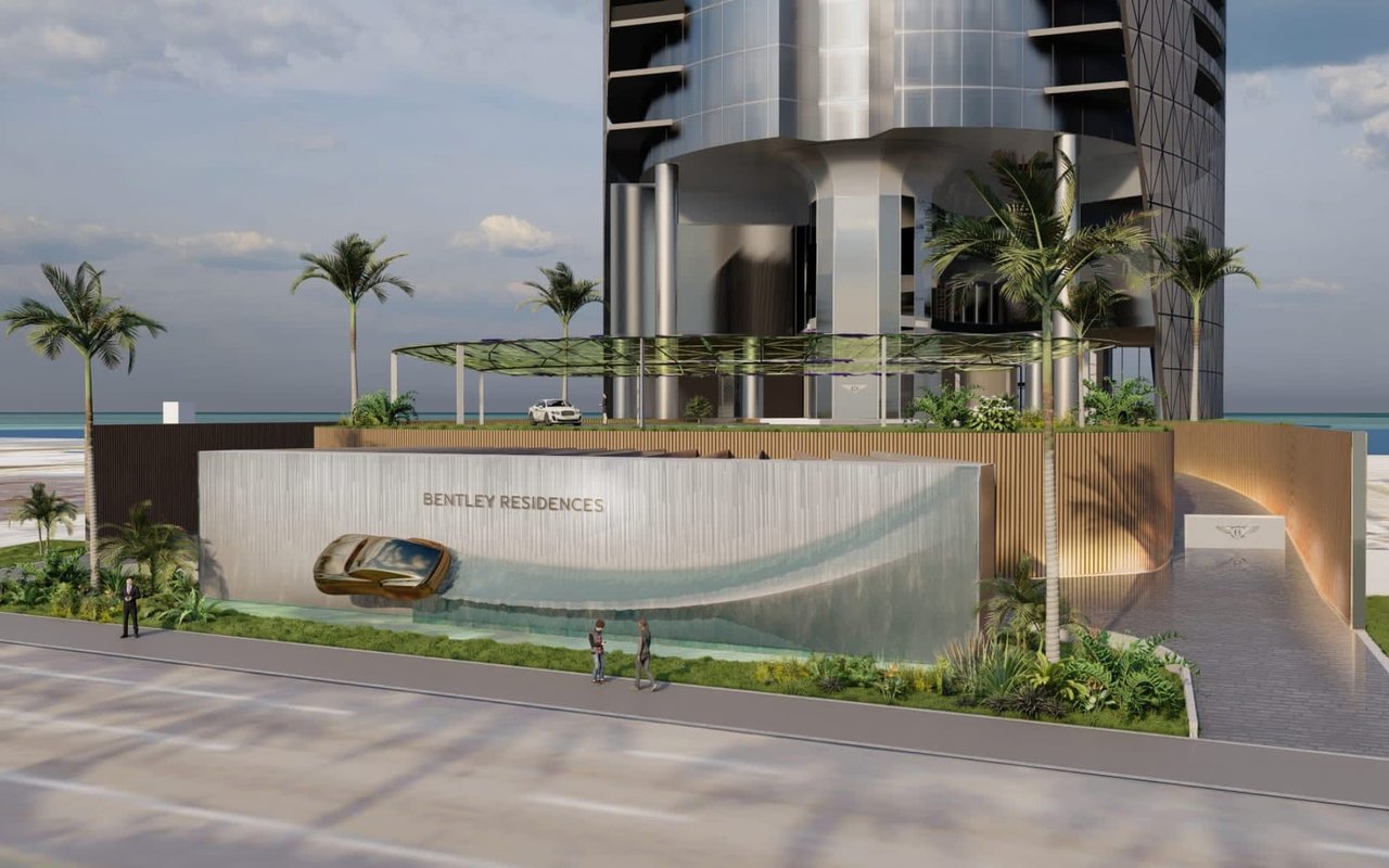 Bentley Residences waterfront tower with a glass façade, palm-lined entrance, and ocean behind it.