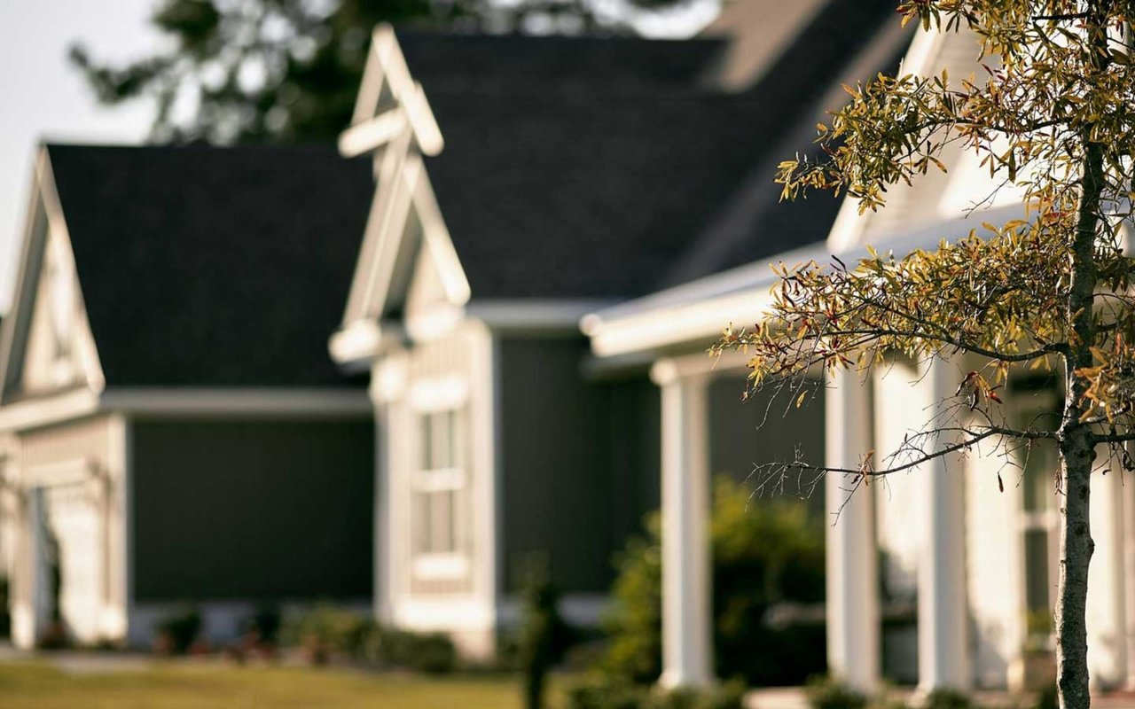 A row of suburban houses with yellow leaves is in the foreground.