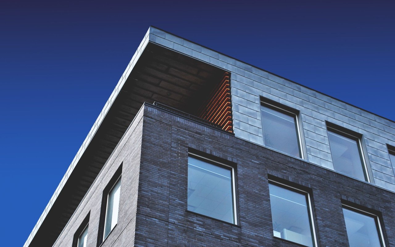 Modern building with dark brick, silver cladding, large windows, and a deep roof overhang.