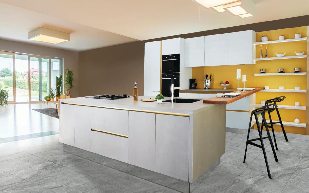  A sleek, modern kitchen with a large light gray island in the foreground, featuring a sink, stovetop, and gold accents. 