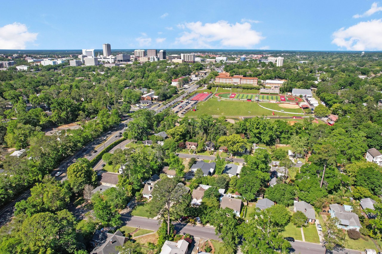 An aerial view of a residential area, showing houses, streets, and trees with a view extending to a distant urban skyline.