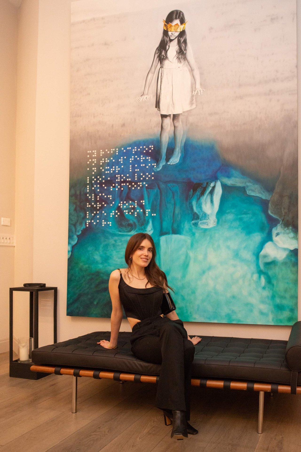 Woman in black seated before a large turquoise mural of a crowned figure.