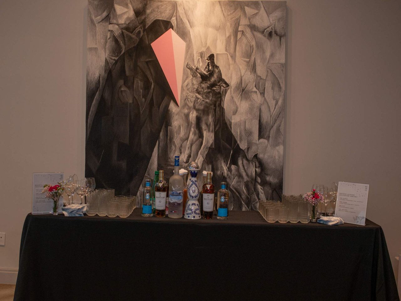 Event drinks station with bottles and glasses arranged beneath a large abstract painting.