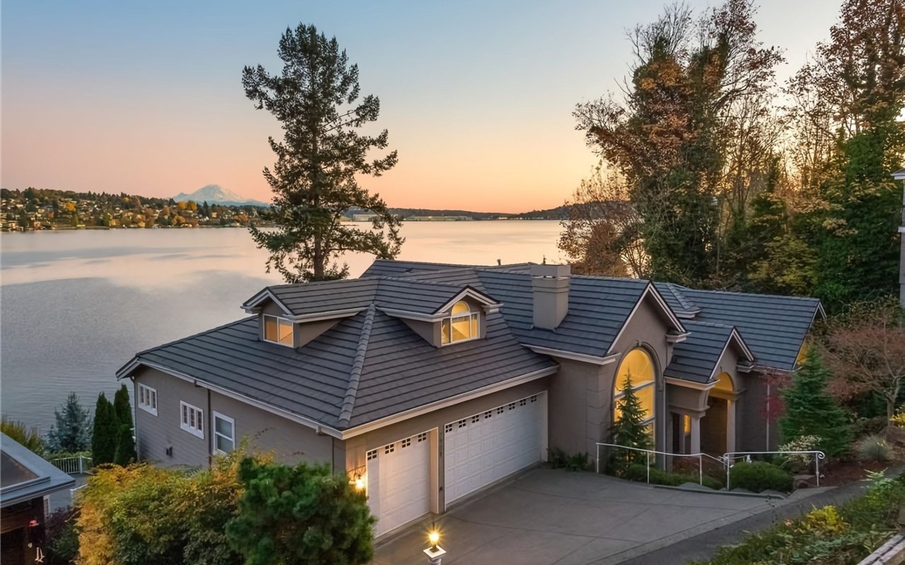 A modern house with a two-car garage attached. The house has windows facing a lake.