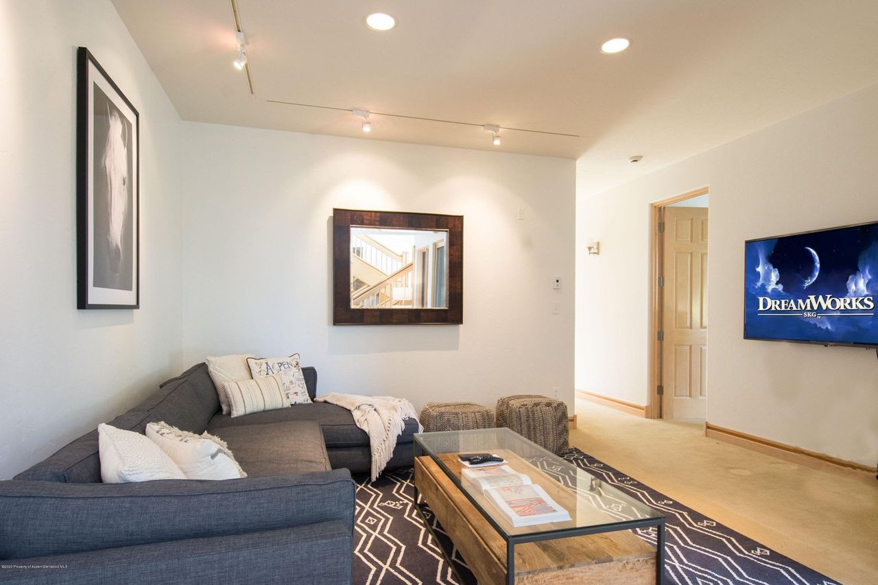 Living room with a gray sectional, patterned rug, wooden coffee table, and wall-mounted television.