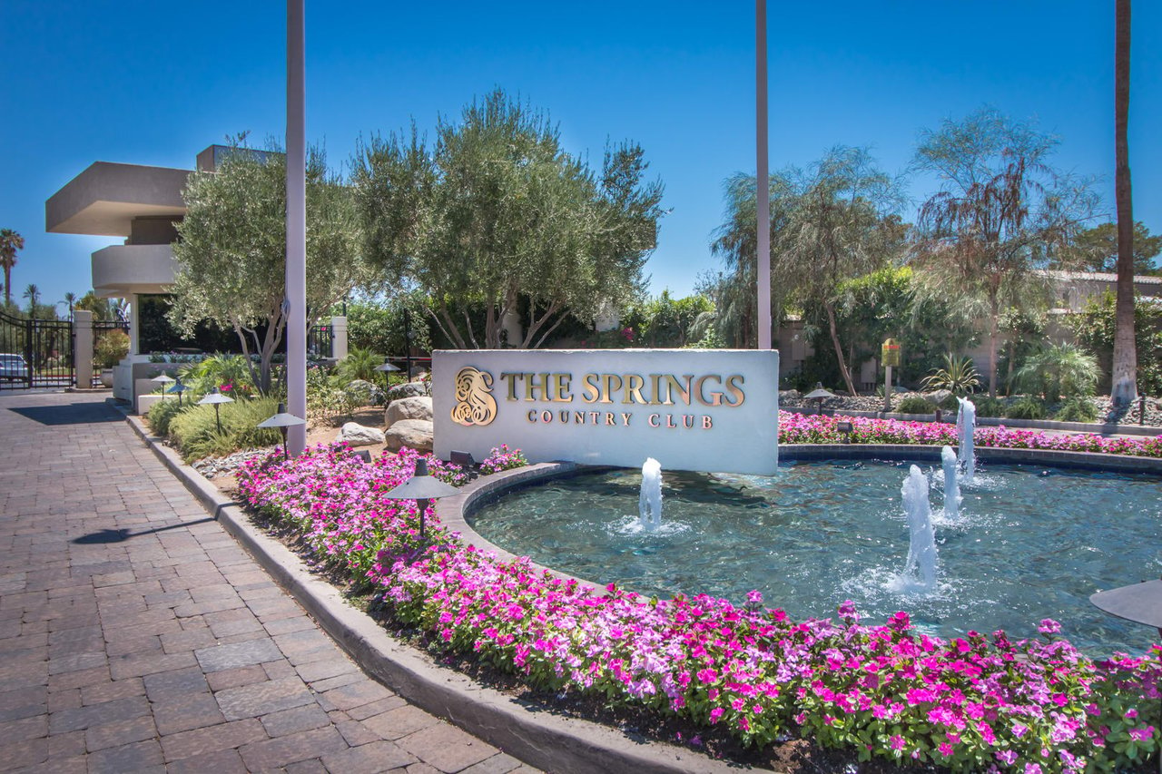 The Springs Country Club entrance with a fountain and a stone sign in the foreground.