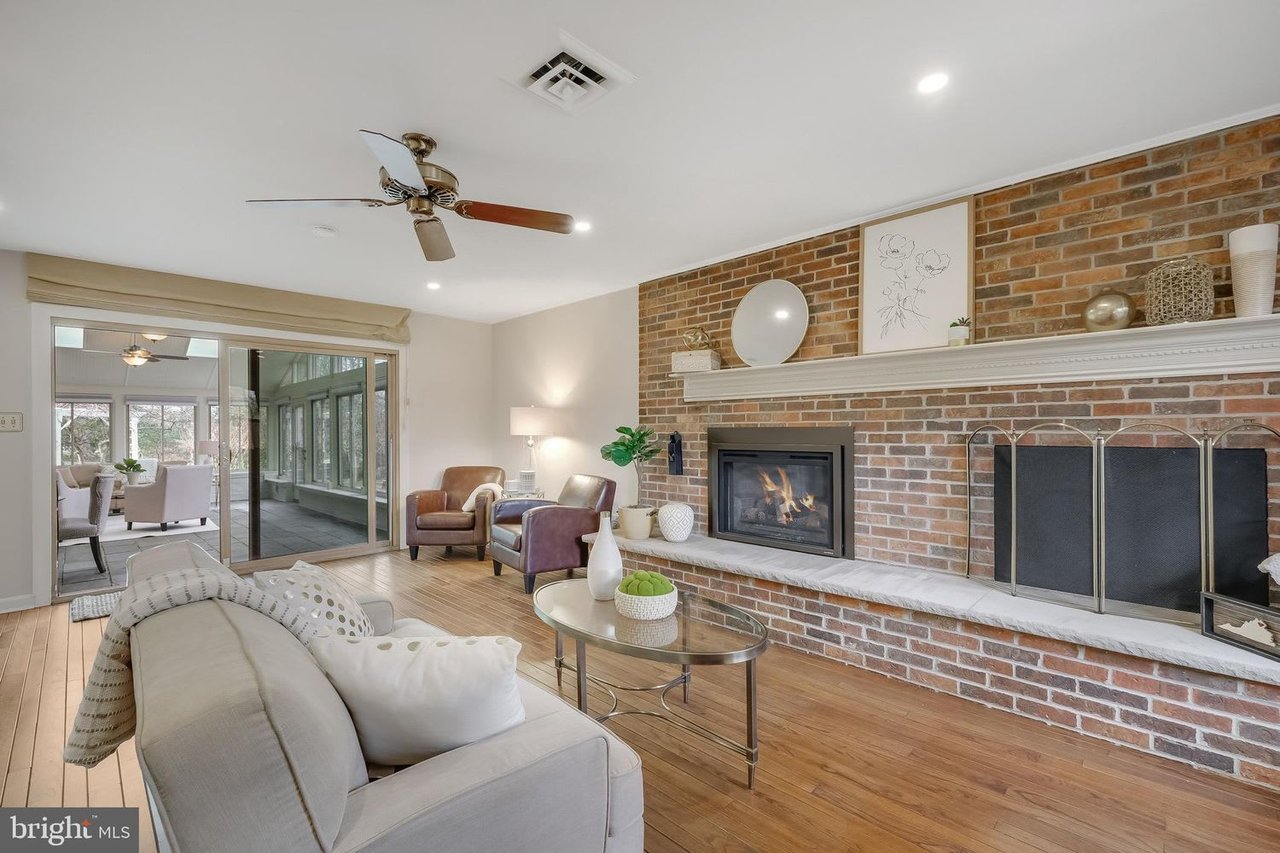 Living room with a brick fireplace, hardwood floors, and sliding doors to a sunroom.