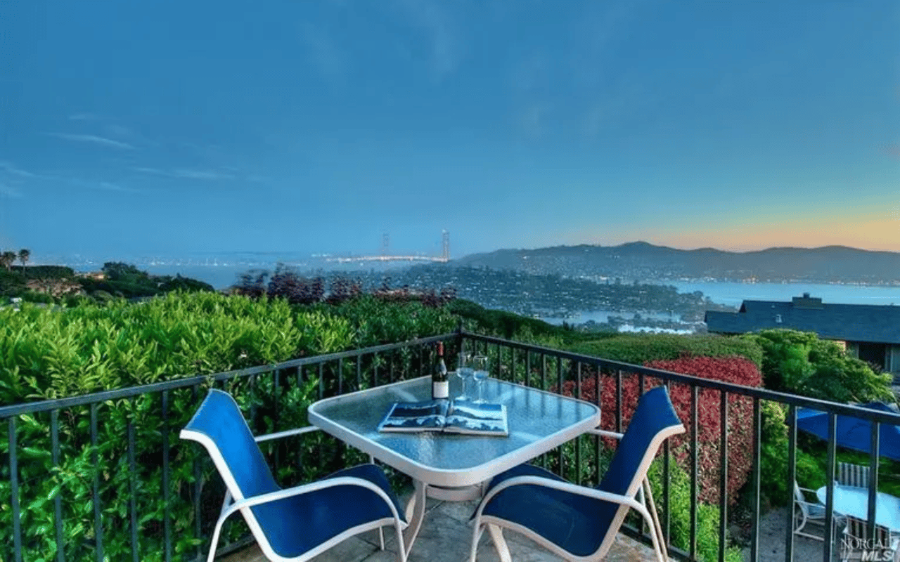 Panoramic view of a city skyline and bridge from a cozy balcony with a table setting.