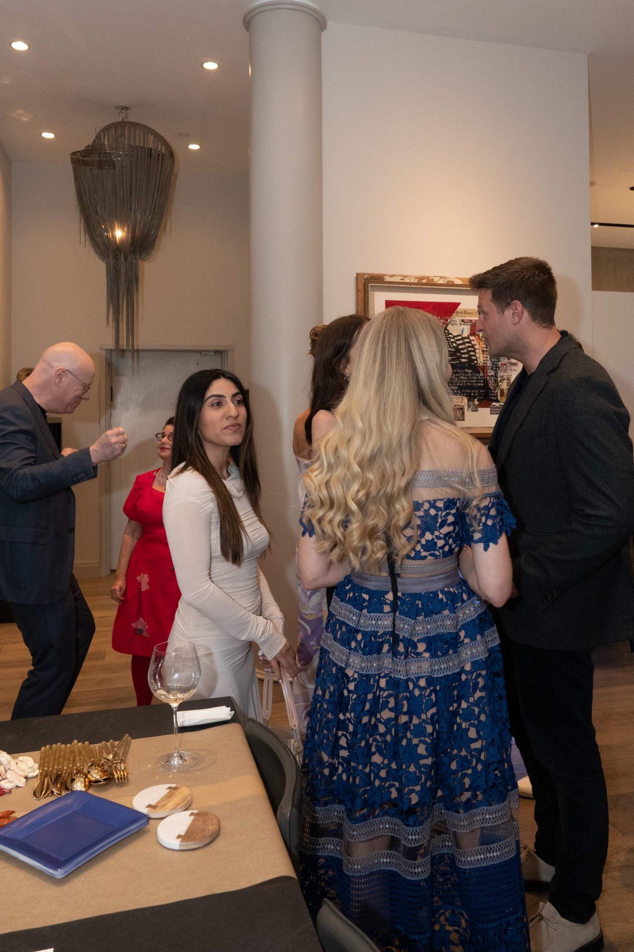 Guests mingle beside a table set for an event in a warmly lit interior.