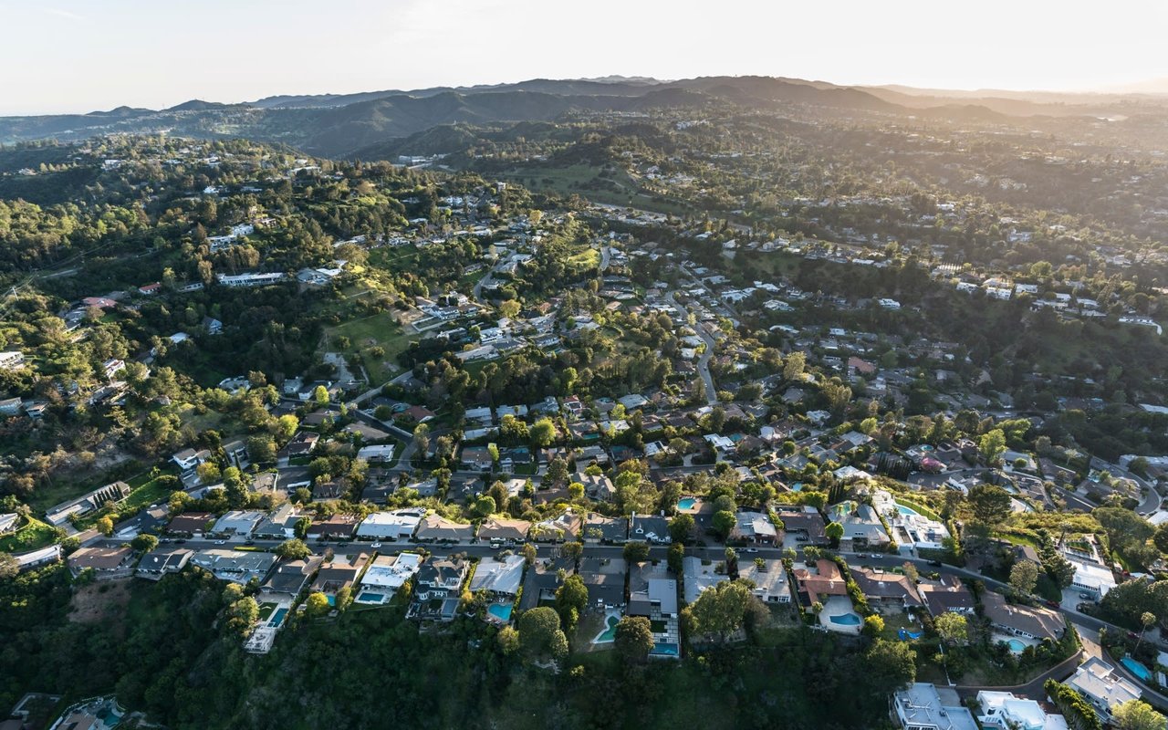 An aerial view of a suburban neighborhood with winding streets and colorful houses with big backyards.