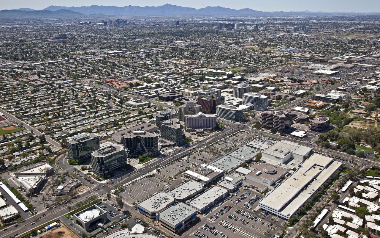 An aerial view of a city with tall buildings, parking lots, and mountains in the background