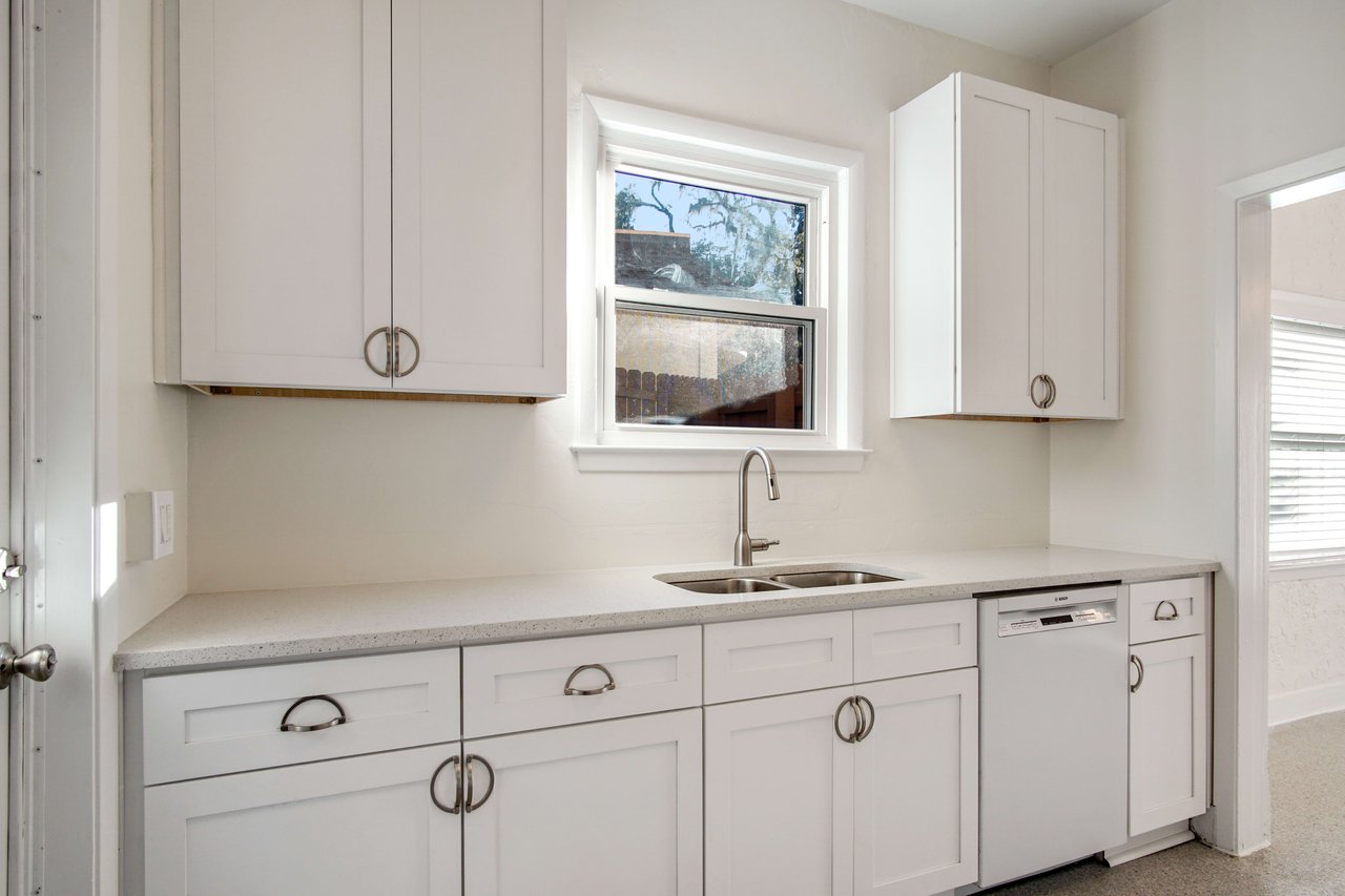 Another view of the kitchen, focusing on the area near the oven and sink. The kitchen has white cabinets and a window above the sink.