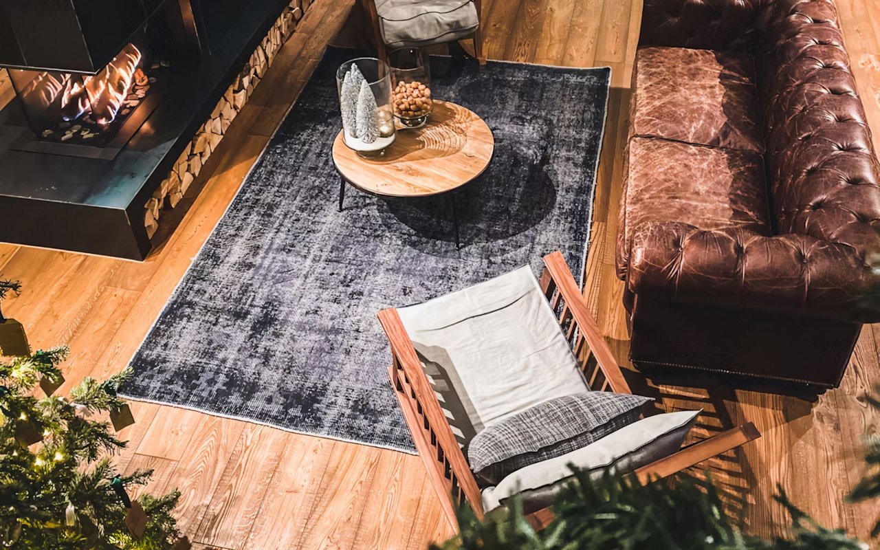  Cozy living room with a fireplace, leather sofa, wooden chairs, and a dark blue rug.