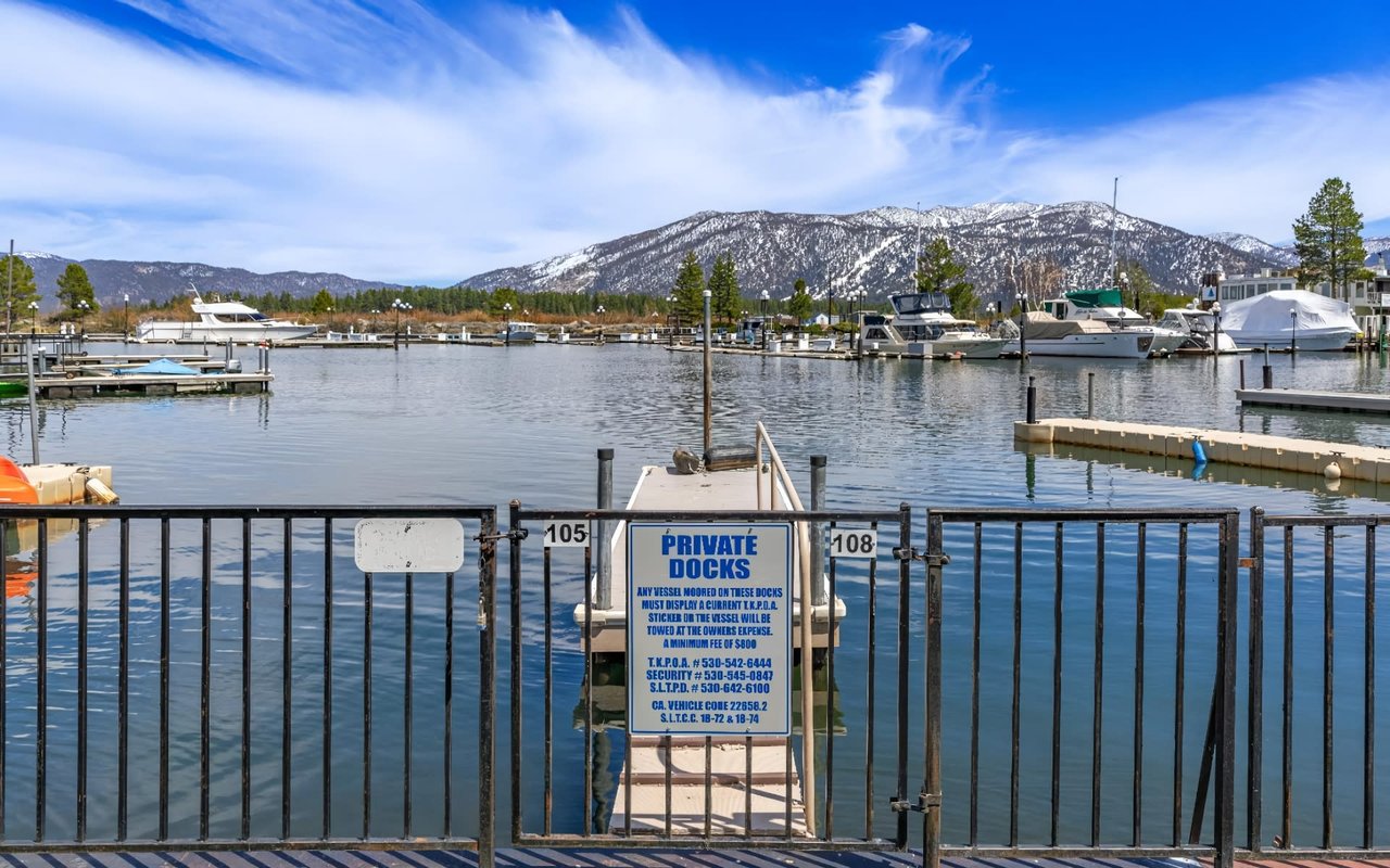 Tranquil marina scene with clear blue skies, snow-capped mountains, and calm water.