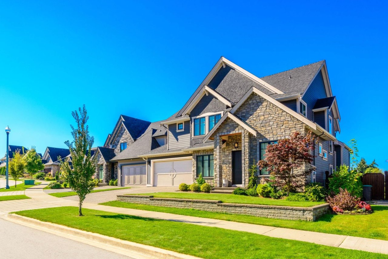 A large house with brick walls and a lush green yard on a sunny day with a blue sky.