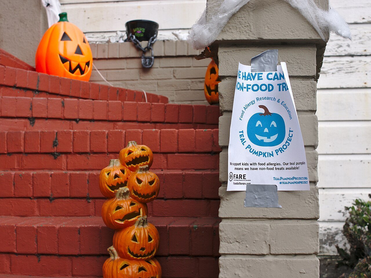 A Teal Pumpkin Project sign taped to a porch beside jack-o'-lanterns