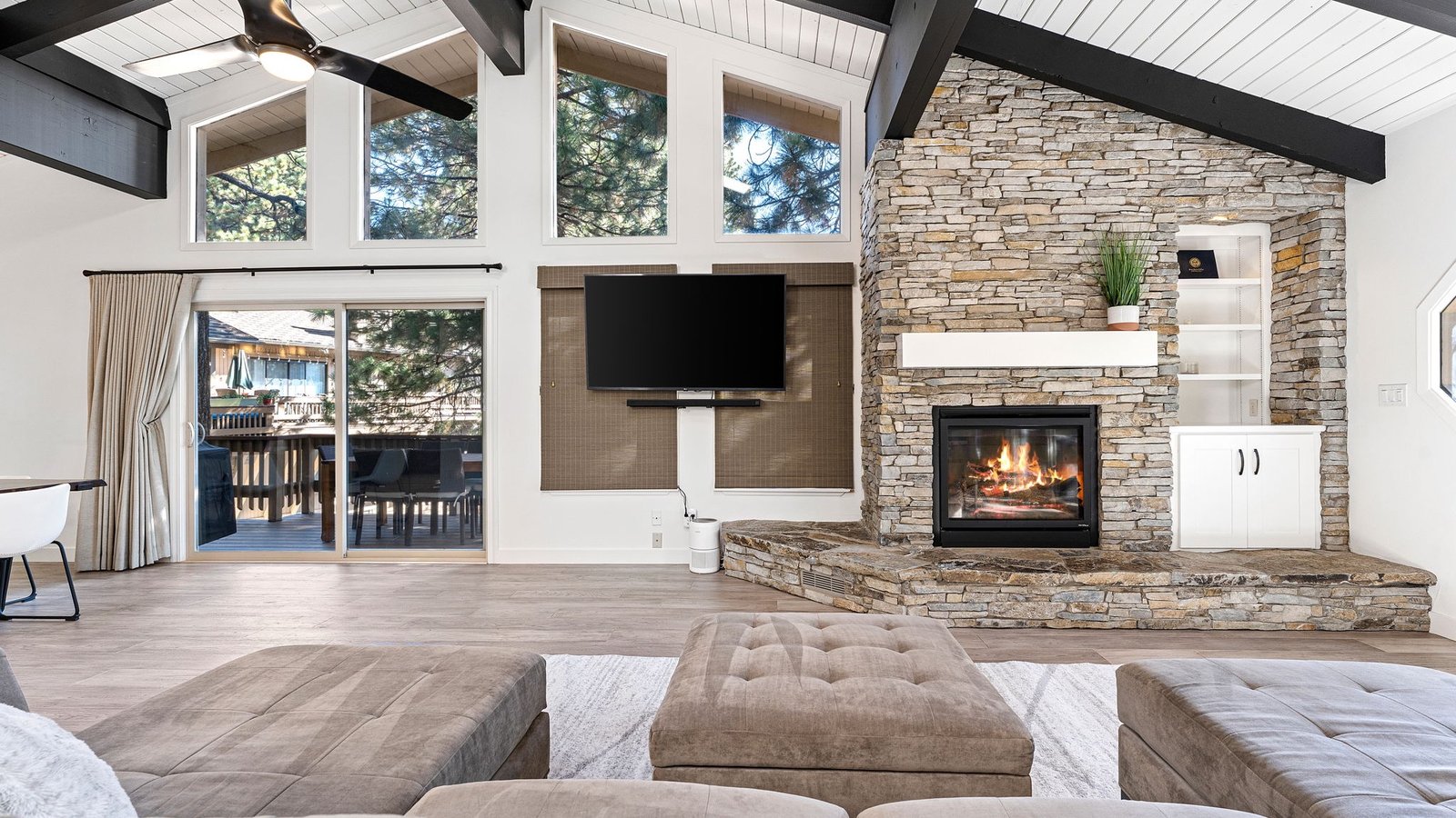 Vaulted great room with a stone fireplace, dark beams and tall windows to the pines in a White Pines condominium