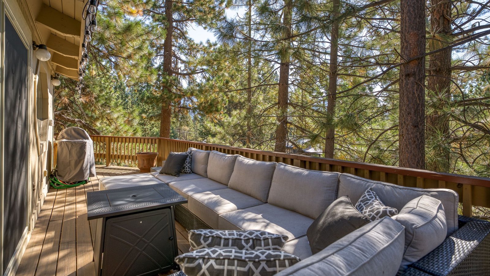 Deck with an outdoor sectional sofa and fire table among tall pines at a White Pines condominium on Oriole Way