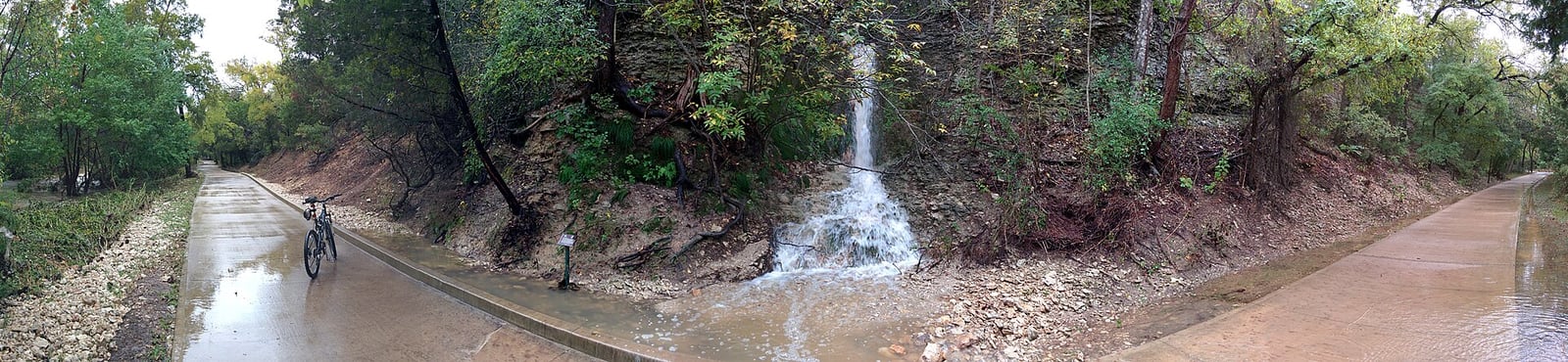 Concrete trail along Brushy Creek beside a small limestone waterfall in Cedar Park