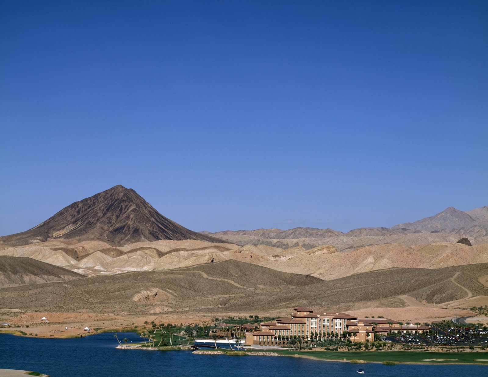 Lakeside resort with terracotta roofs and palm trees on the shore of Lake Las Vegas, with a dark volcanic peak and desert hills behind it