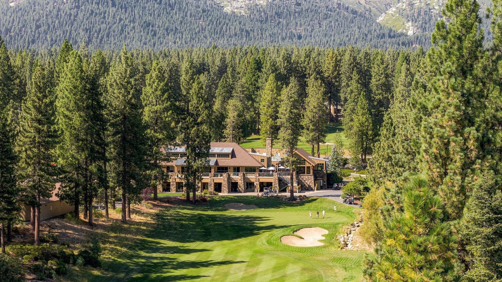 The Chateau clubhouse behind a green and sand bunker on the Championship Golf Course in Incline Village, with golfers on the green and pines all around