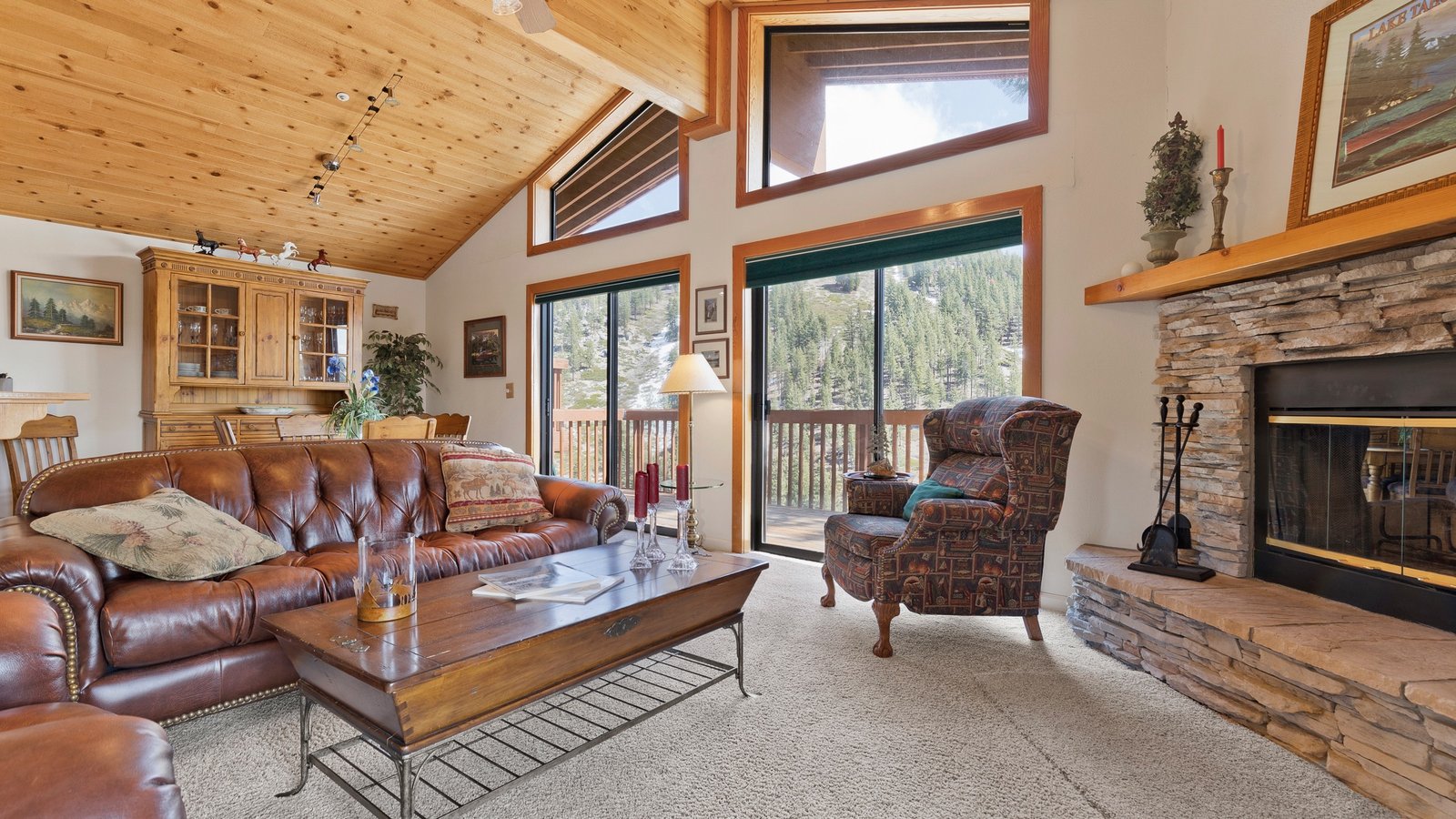 Living room with a vaulted wood ceiling, a stone fireplace and tall windows to the pines in a Bitterbrush townhome