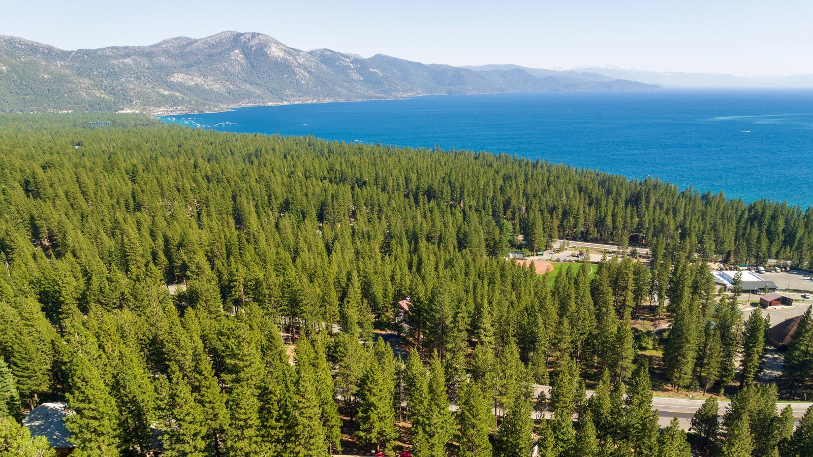 Aerial view over a pine forest with homes tucked among the trees in Lower Tyner, Incline Village, with deep-blue Lake Tahoe and mountains beyond