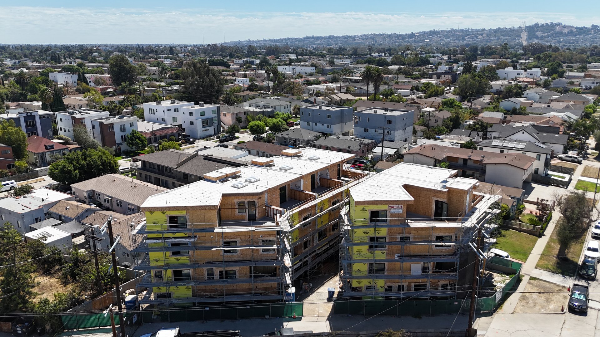 Aerial view of multifamily buildings under construction amid a dense residential neighborhood.