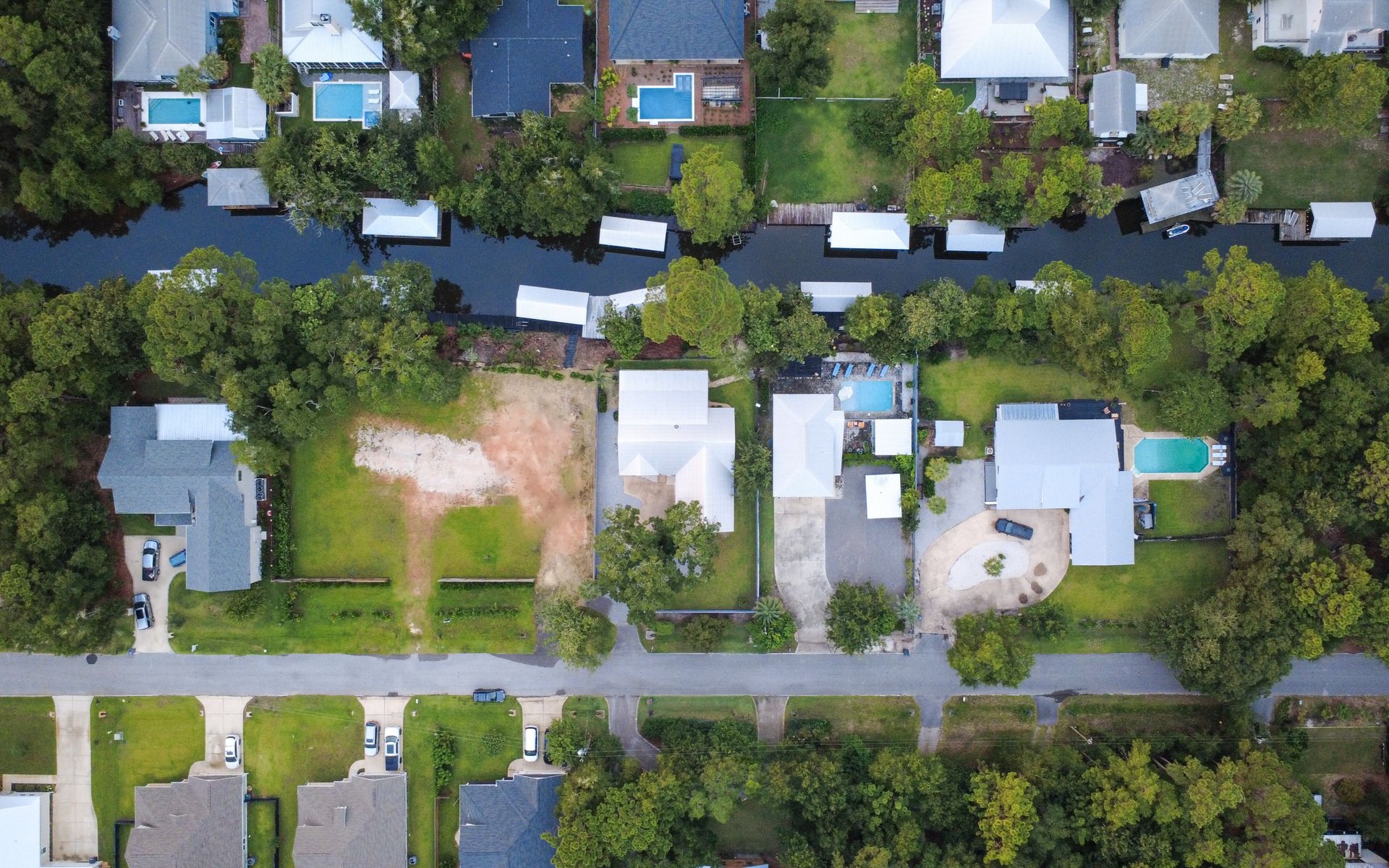 Aerial view of a cleared lot and neighboring homes beside a tree-lined canal.