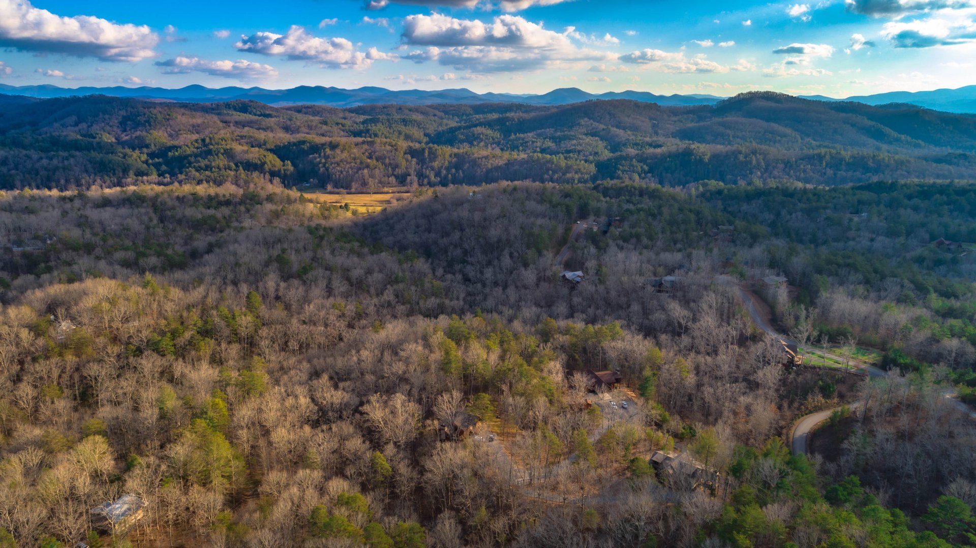 Aerial view of wooded mountain ridges with scattered cabins and winding roads.