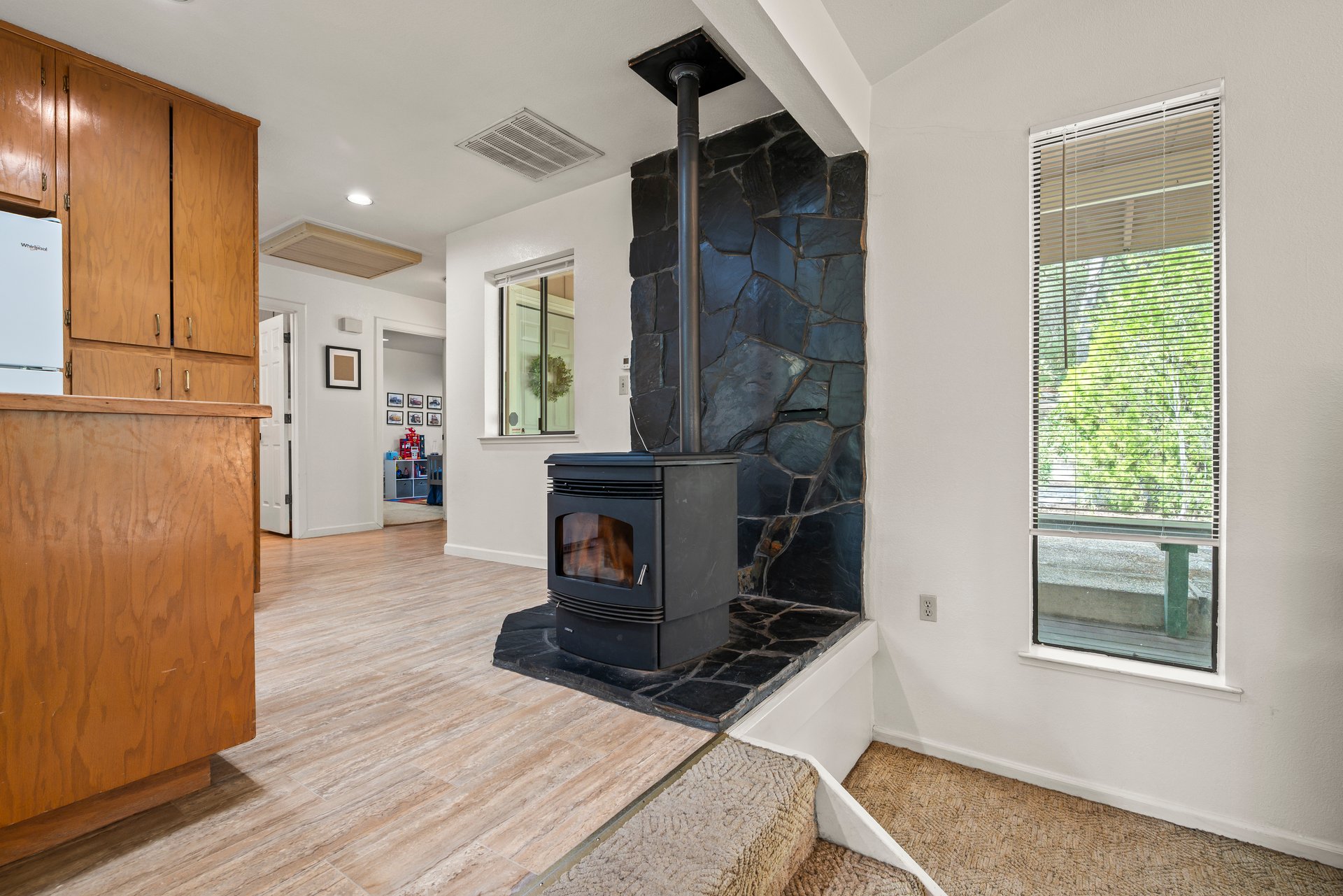 Kitchen with wood cabinets and a black wood stove against a dark stone hearth.