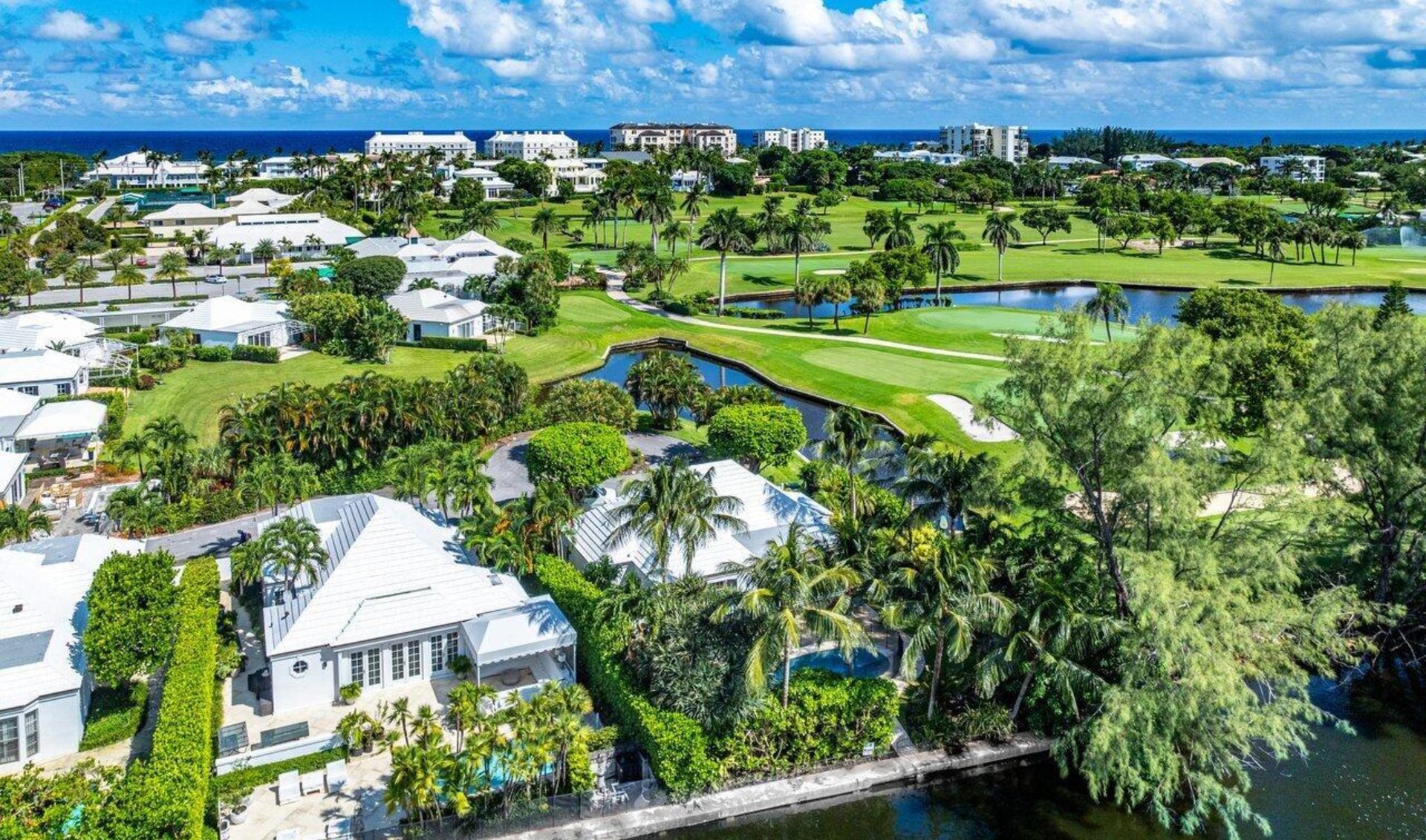 Aerial view of palm-lined homes and a golf course beside the ocean.
