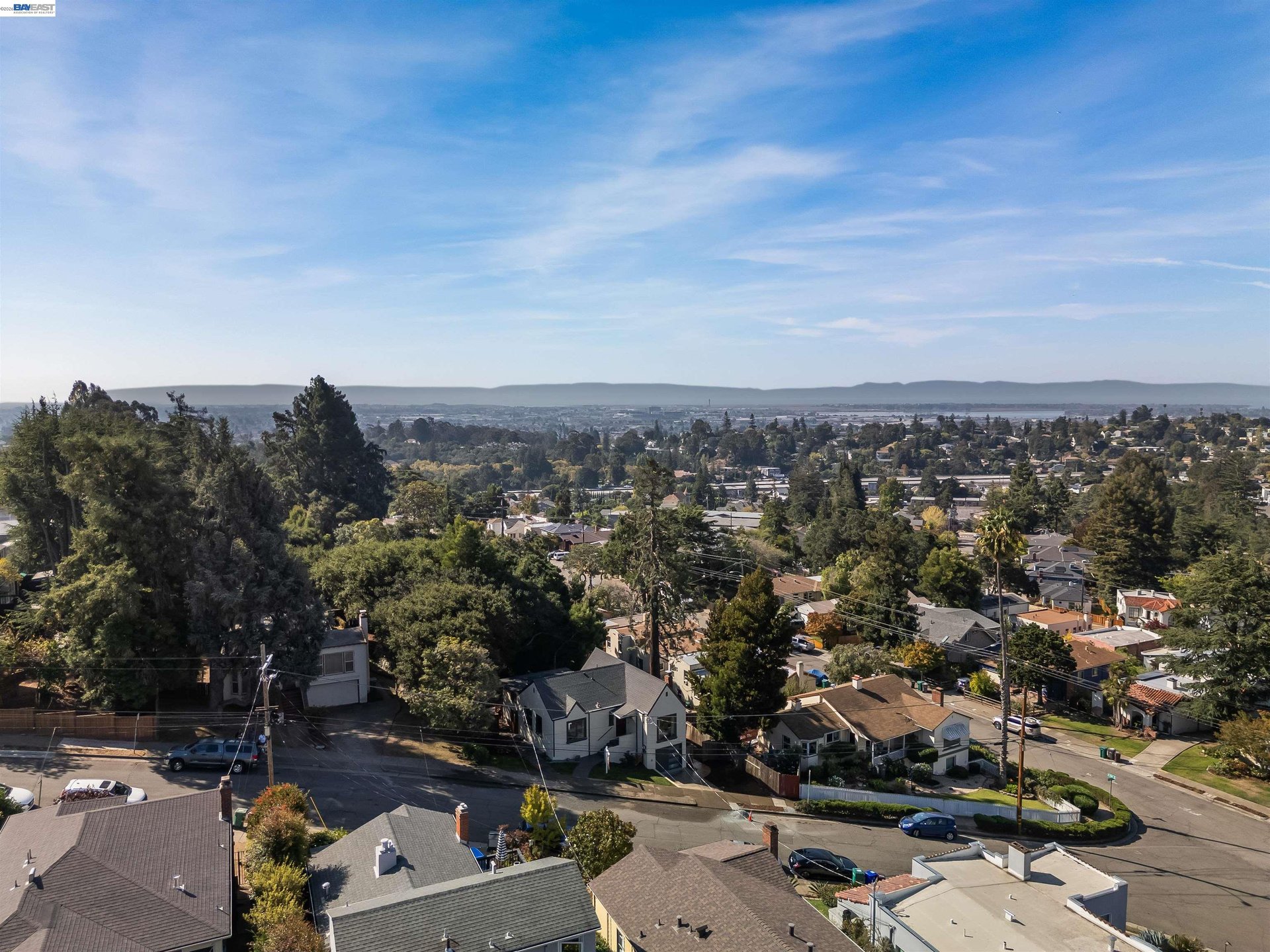 Panoramic Oakland neighborhood view with the bay and distant hills beyond the rooftops.